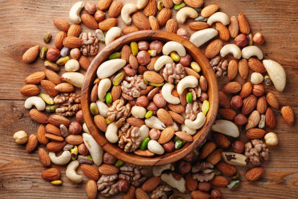 Wooden bowl with mixed nuts on rustic table top view. Healthy and nutrient food and snack.